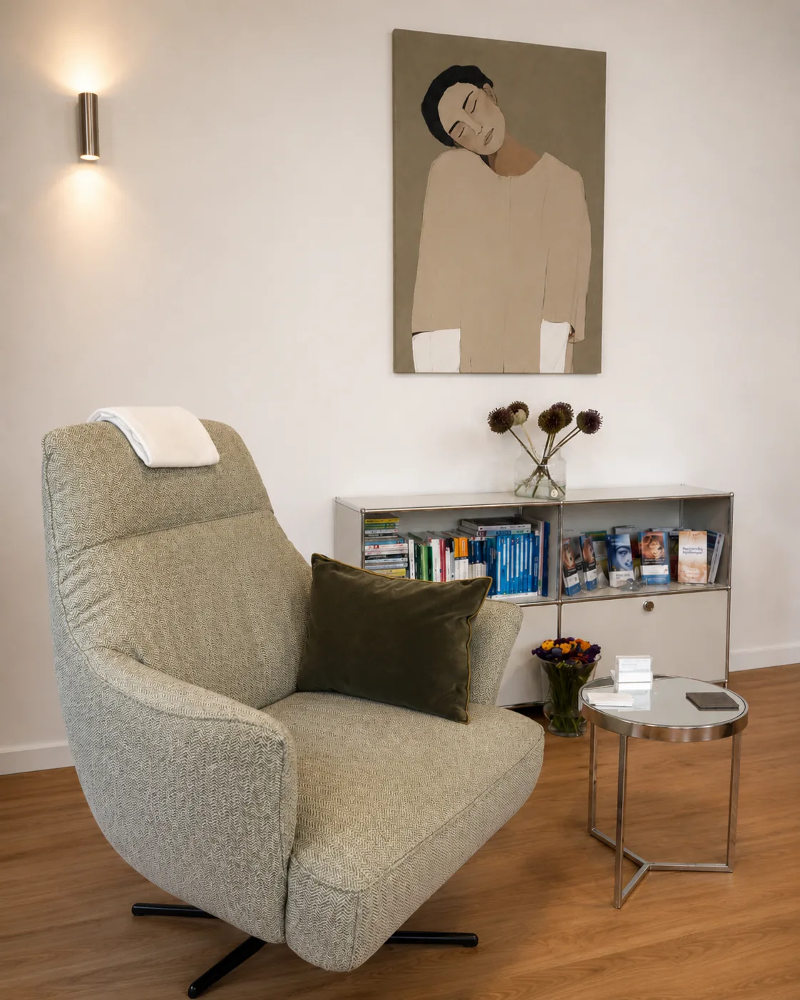 Sessel mit Wandbild, Leuchte und kleinem Beistelltisch im Behandlungsraum.